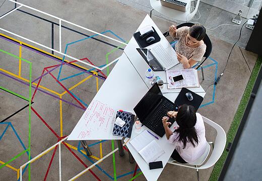 Zwei Frauen arbeiten an Laptops am Schreibtisch, repräsentieren Website-Betreiber, die auf die Google-Updates 2023 reagieren