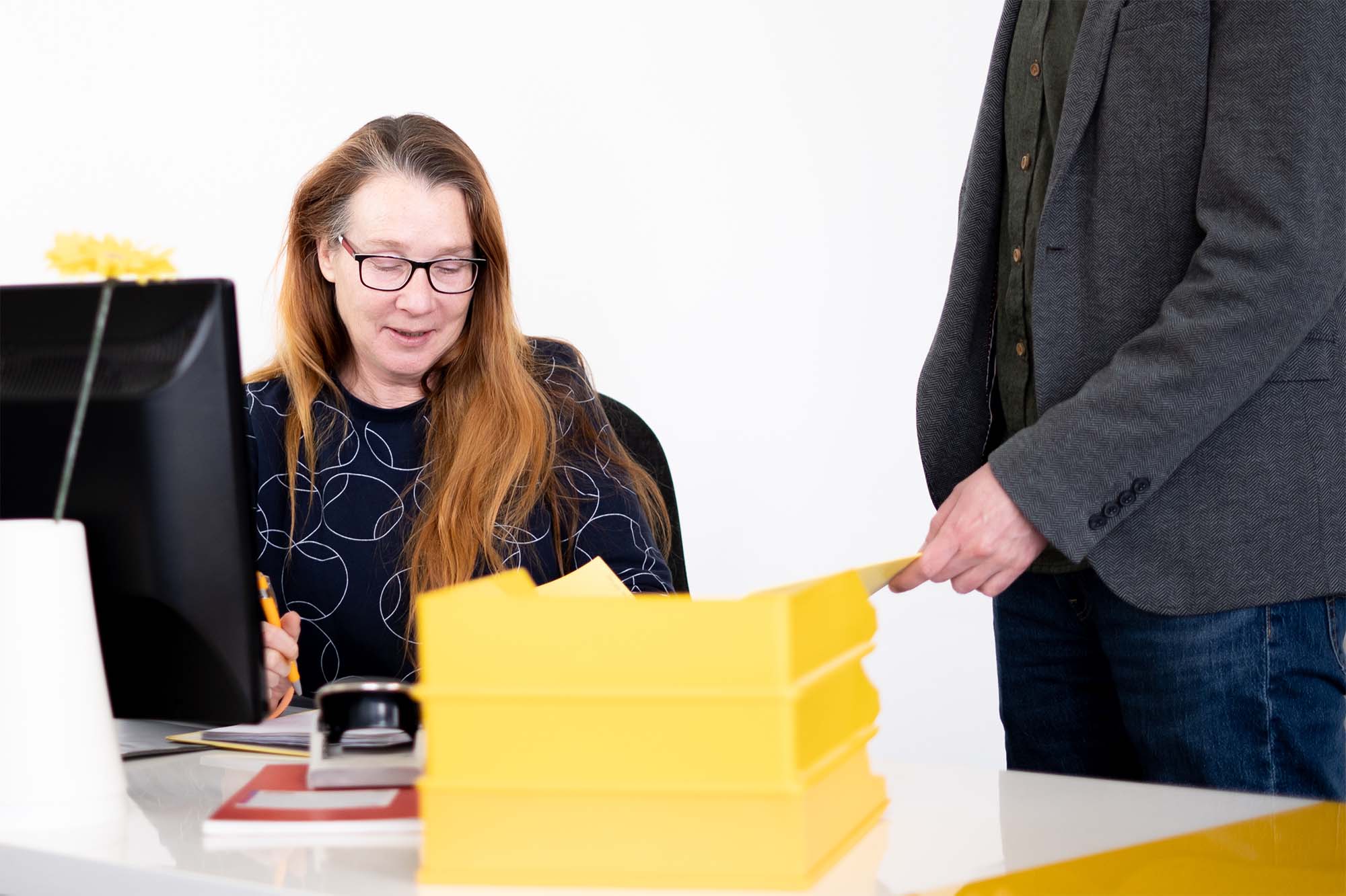 Abstimmung in der Buchhaltung: Mitarbeiterin bespricht Unterlagen mit Kollegen am Schreibtisch.