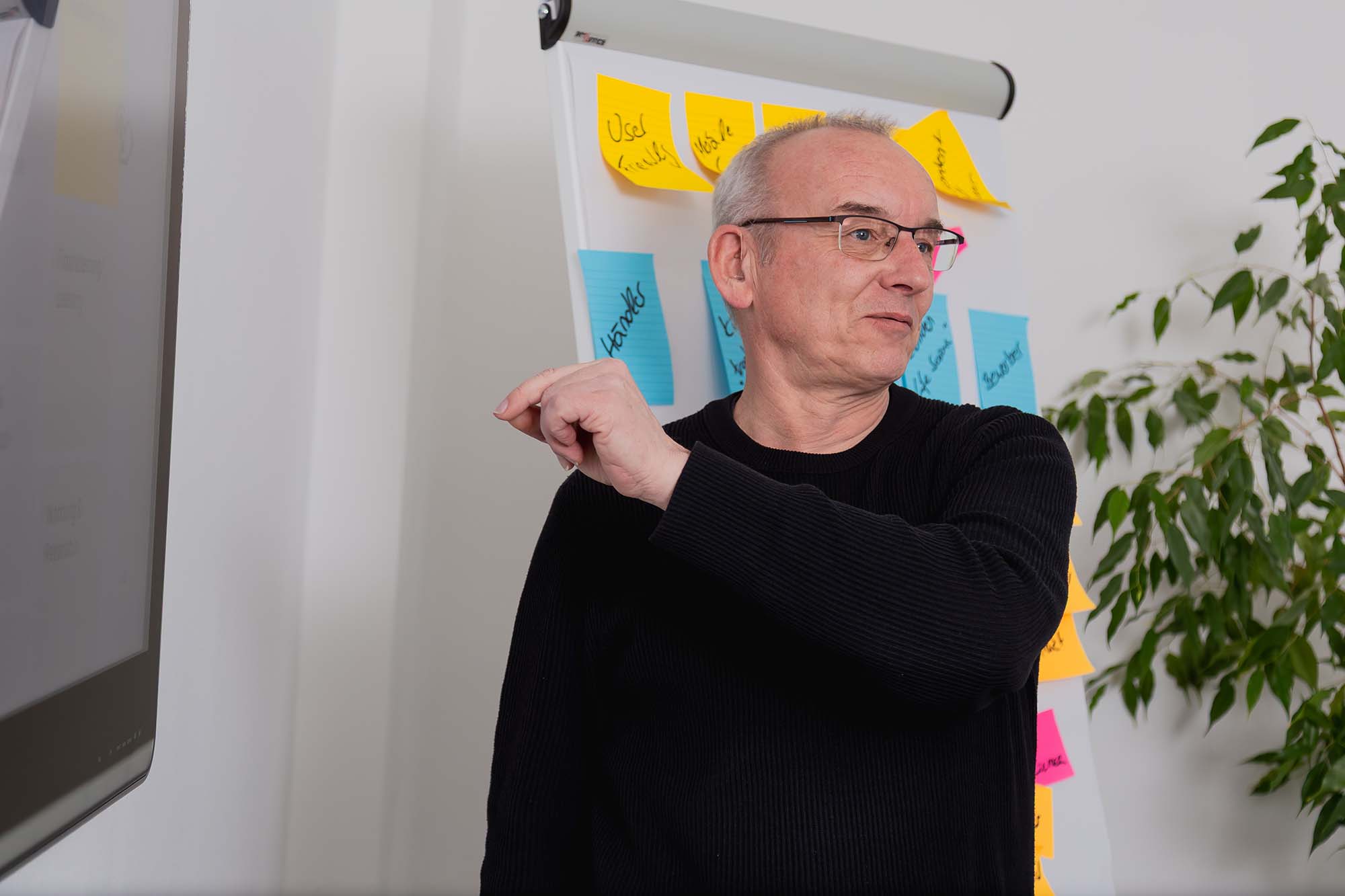 Digitalagentur erklärt die Projektstrategie am Whiteboard mit Haftnotizen in einem modernen Büro.