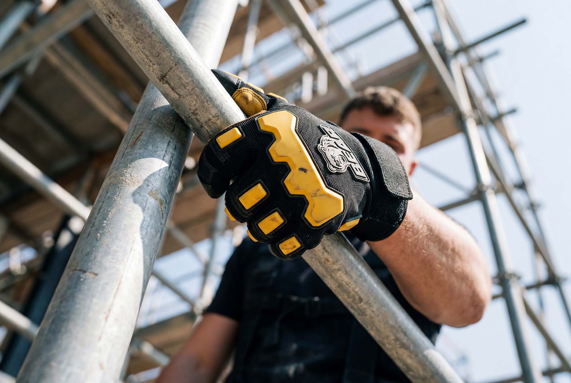 Hand eines Arbeiters am Gerüst Nahaufnahme einer Hand in einem schwarz-gelben Schutzhandschuh, die ein Metallrohr auf einer Baustelle greift.