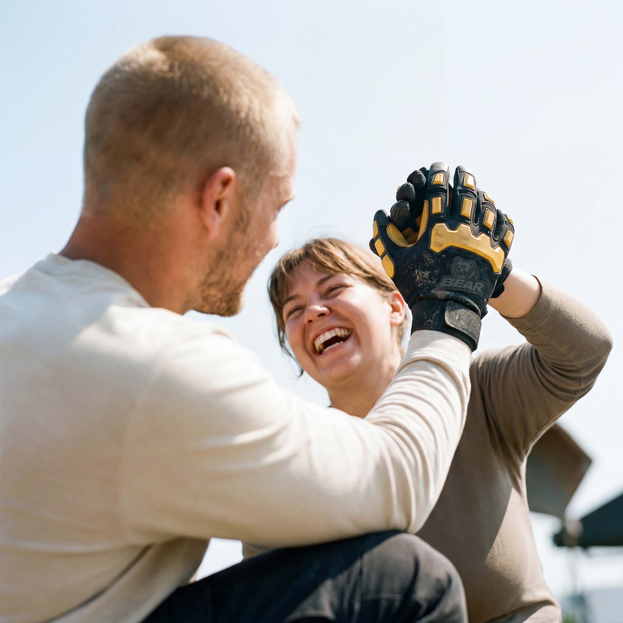 Fröhlicher High-Five nach der Arbeit Mann und Frau geben sich High-Five. Frau trägt Arbeitshandschuh, lacht. Heller Himmel im Hintergrund.