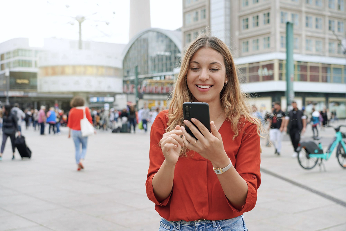 Frau nutzt unterwegs in der Innenstadt ihr Smartphone zur Informationssuche – Beispiel für Mobile First Internetnutzung.
