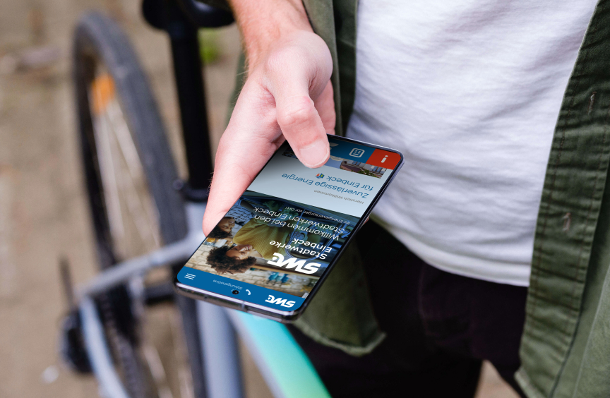 Hand hält ein Smartphone mit geöffneter Stadtwerke-Einbeck-Website neben einem Fahrrad im Außenbereich