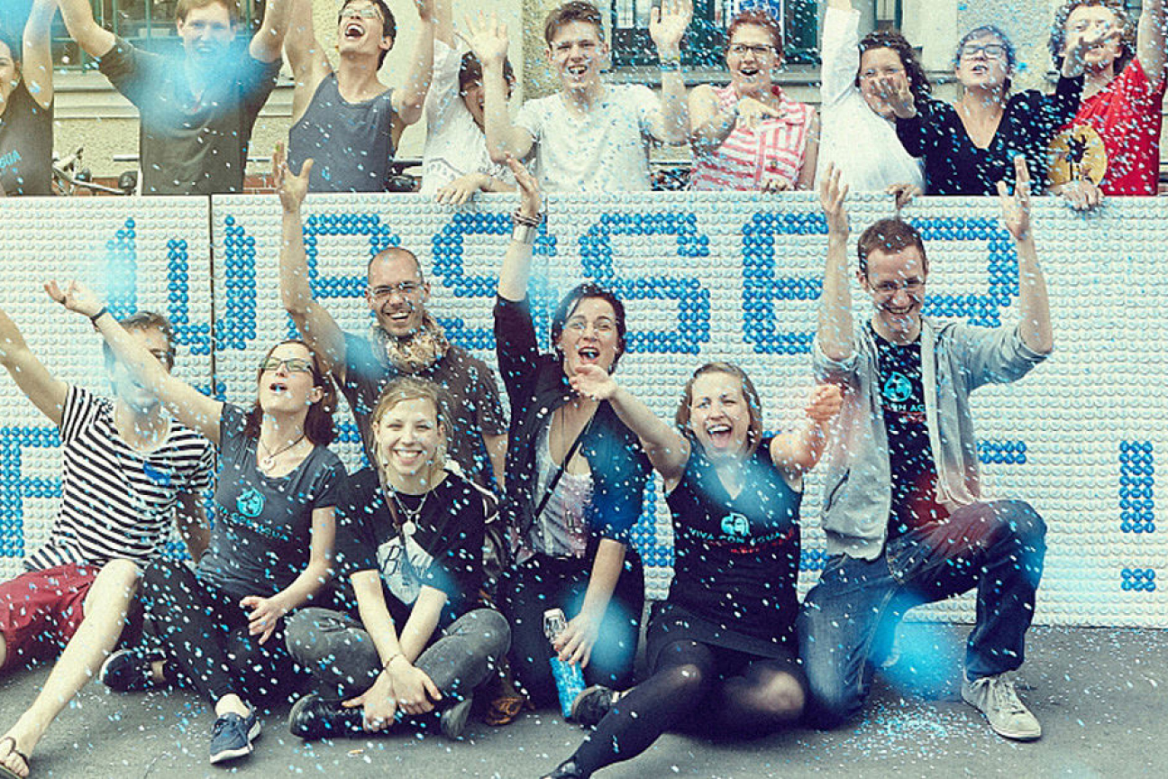 Jubelnde Gruppe vor einer Wand mit Schriftzug „Wetten für Wasser“ und blauem Konfetti